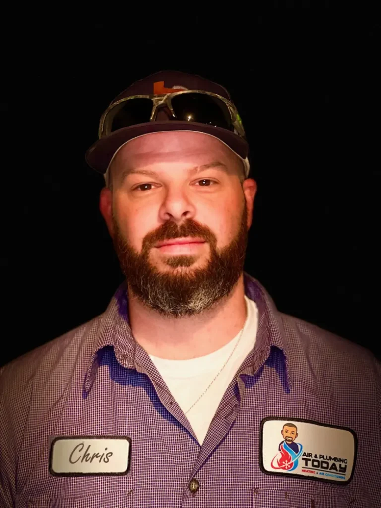 A man with a beard wearing a purple checkered shirt, baseball cap, and sunglasses on his head. His shirt has name tags reading "Chris" and "Air & Plumbing Today," perfect for an about us introduction.