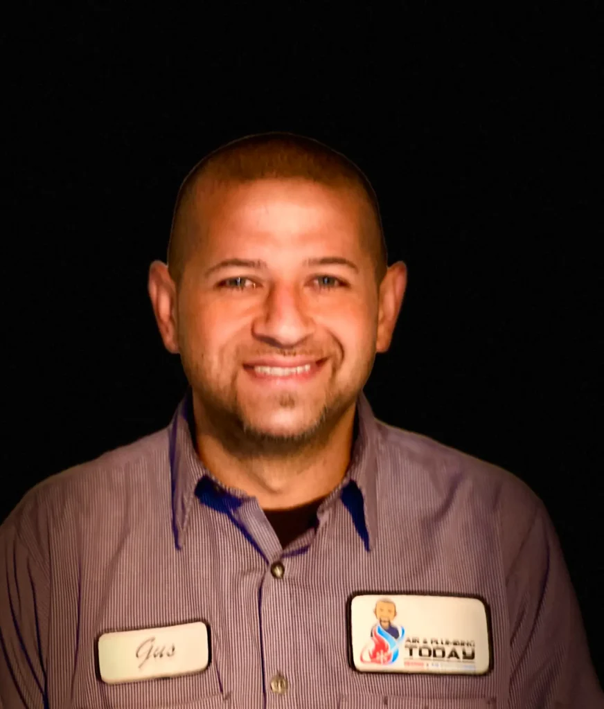 A man wearing a striped work shirt with name tags, smiling and facing the camera against a black background, perfectly captures the friendly spirit of our About Us page.