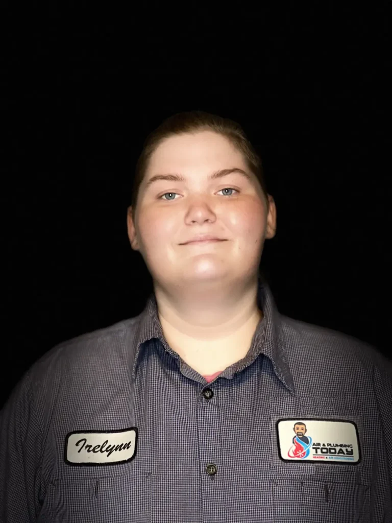 A person with short hair wearing a checkered work shirt with a name tag "Irelynn" and a company logo, posed against a black background, embodies the spirit of our About Us story.