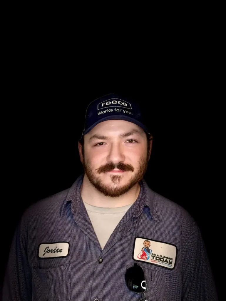 A man with a beard wearing a blue cap and work shirt, name tag reads "Jordan," stands against a black background—ready to represent our team on the About Us page.