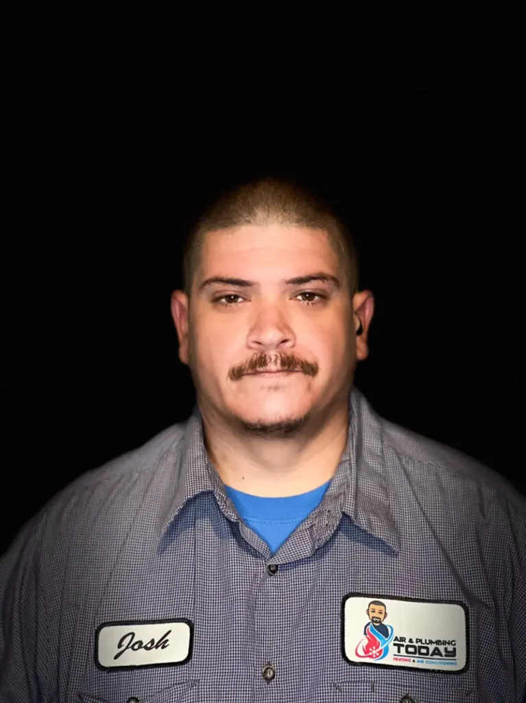 A man with short hair and a mustache, wearing a checkered work shirt with name and company patches, stands against a black background—perfect for your "about us" page to showcase team authenticity.