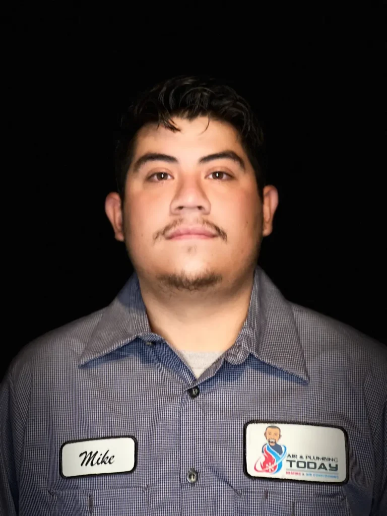 A man in a checkered work shirt with a name tag "Mike" and an "AR Plumbing Today" patch, stands against a black background, ready to represent our team. Learn more about us and our commitment to quality service.