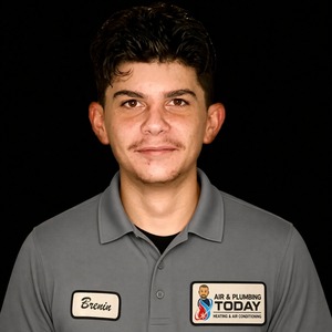 A young man with short dark hair wearing a gray polo shirt with company logos and a name tag stands against a plain black background, representing our dedicated team featured on the about us page.