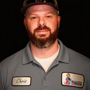 A man with a beard wearing a gray polo shirt, cap, and sunglasses on his head stands against a black background. His shirt features name and company patches, perfectly embodying the professional spirit of our “about us” story.