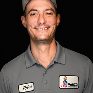 A man wearing a gray polo shirt and cap with “Robert” and “Air & Plumbing Today” name patches, smiling against a black background—ready to represent our team and share more about us.